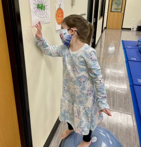 Child on balance ball with a picture of a spider web with green play-doh spider family at The Hello Clinic gym.. 